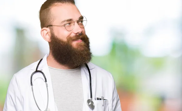 年轻的金发医生留着胡子 穿着医用外套 面带微笑地看着身边 自然表情 笑自信 — 图库照片