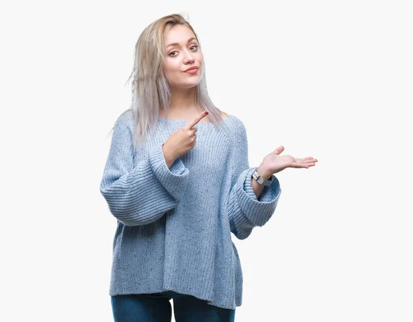 驚くし 手とを提示 指で指している間カメラに笑顔孤立の背景に冬のセーターを着ている若いブロンドの女性 — ストック写真