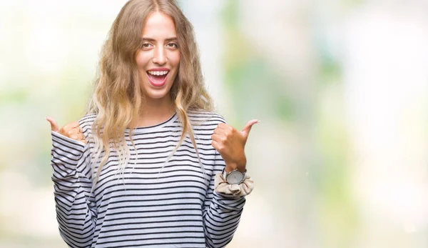 Beautiful young blonde woman wearing stripes sweater over isolated background success sign doing positive gesture with hand, thumbs up smiling and happy. Looking at the camera with cheerful expression, winner gesture.
