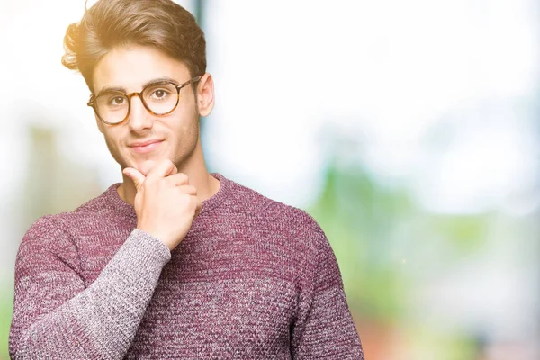 Young handsome man wearing glasses over isolated background looking confident at the camera with smile with crossed arms and hand raised on chin. Thinking positive.