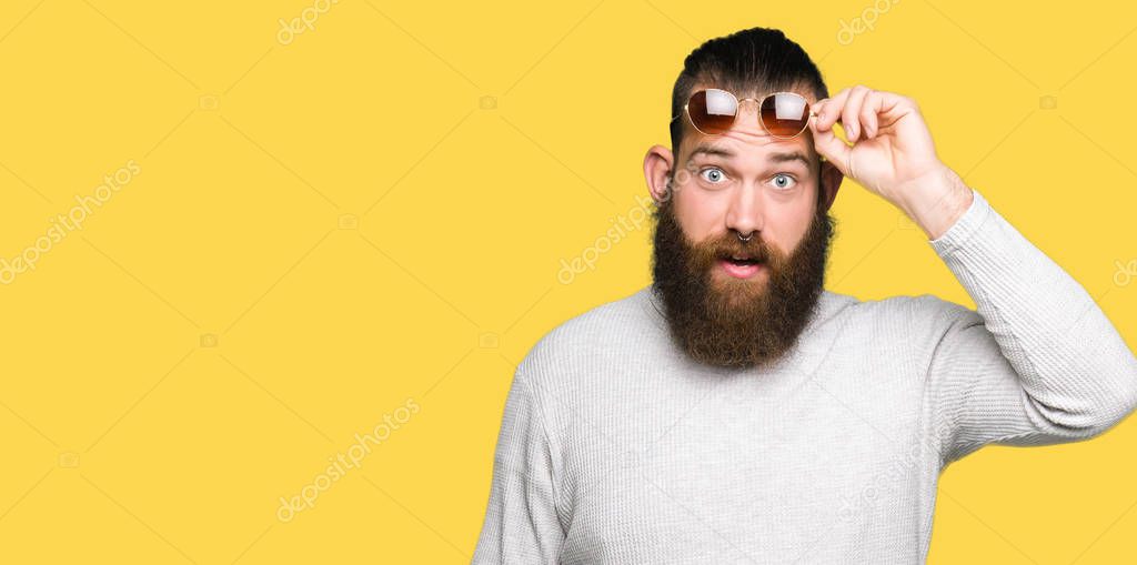 Young hipster man wearing sunglasses afraid and shocked with surprise expression, fear and excited face.