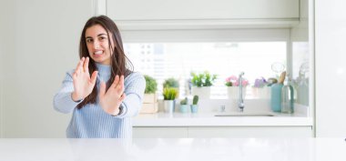 Güzel genç kadın evde beyaz masaya oturan geniş açı resim tiksinti ifadesi, memnun ve korkulu tiksinti yüz yapıyorsun çünkü nefret tepki. Elleriyle kaldırdı. Sinir bozucu kavramı.