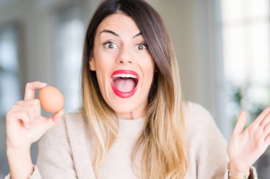 Evde çok mutlu ve heyecanlı, taze yumurta tutan genç güzel kadın büyük gülümseme ile çığlık ve ellerini kaldırdı kazanan ifade kutluyor zafer