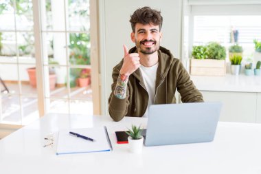Ok işareti, başparmak ile parmak, mükemmel işareti yapıyor kocaman bir gülümseme ile bilgisayar laptop ve defter mutlu kullanan genç öğrenci adam