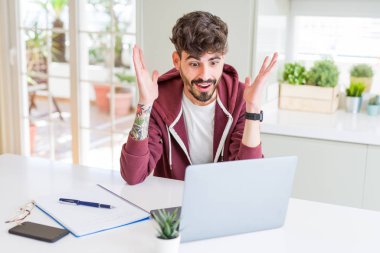 Bilgisayar laptop ve defter çok mutlu ve heyecanlı, kullanan genç öğrenci adam kazanan ifade büyük gülümseme ile çığlık ve ellerini kaldırdı zaferini kutluyor