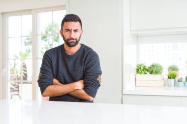 Yüz çapraz kolları olan ev kuşkucu, rahat kazak ve sinir, onaylamayan ifade giyen yakışıklı İspanyol adam. Negatif kişi.