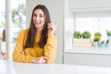 Kameraya bakarak yan el ve parmak ile işaret yüzünde, kocaman bir gülümseme ile sarı kazak giyen güzel genç kadın.