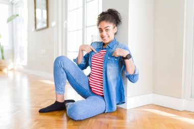 Yüzünde gülümseme ile kendinden emin görünüyorsun, kendini gururlu ve mutlu parmakları ile işaret katta oturan afro saçlı güzel genç Afro-Amerikan kadın.