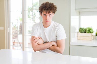 Genç yakışıklı giyen beyaz t-shirt ev şüpheci ve sinir, onaylamayan ifade yüz çapraz kolları olan adam. Negatif kişi.