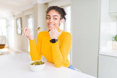 İşaret ve başparmak kadar mutlu yüz gülümseyen tarafı ile gösterilen sağlıklı yeşil siste yeme genç Afro-Amerikan kadın