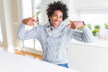 Yüzünde gülümseme ile kendinden emin görünüyorsun, kendini gururlu ve mutlu parmakları ile işaret kış kazak giyen Afrikalı-Amerikalı adam.