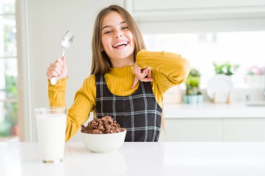 Güzel genç kız çocuk sürpriz ile kahvaltıda çikolata Hububat ve süt yeme yüz kendine işaret parmağı