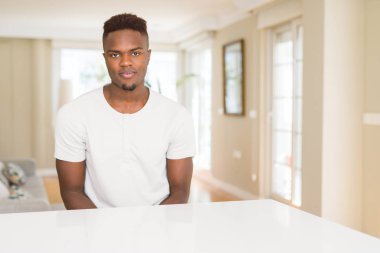 Yüzünde ciddi bir ifade ile yakışıklı Afrikalı-Amerikalı adam evde beyaz masada. Basit ve doğal kameraya bakıyor.