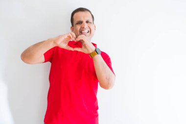Orta yaş adam aşık kalp simgesi ve elleriyle şekil gösteren gülümseyen beyaz duvarın üzerinden kırmızı t-shirt giyiyor. Romantik kavramı.