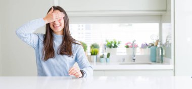 Güzel genç kadın masada gülümseyen ve ile Gülen gözler için sürpriz kapsayan yüz el beyaz evde oturan geniş açı resim. Kör kavramı.