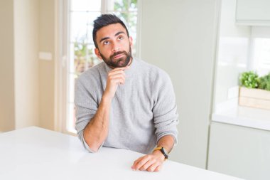 Çene düşünme hakkında soru, dalgın ifade üzerine el ile evde rahat kazak giyen yakışıklı İspanyol adam. Düşünceli yüzüyle gülümsüyor. Şüphe kavramı.