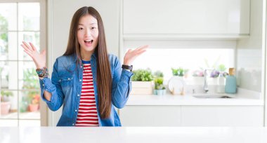 Güzel Asyalı kadın giyiyor denim beyaz masa kutluyor saçma sapan şeylerden ceket ve başarı için kaldırdı Kollarını açarak hayret ve heyecanlı çığlık gözleri açık. Kazanan kavramı