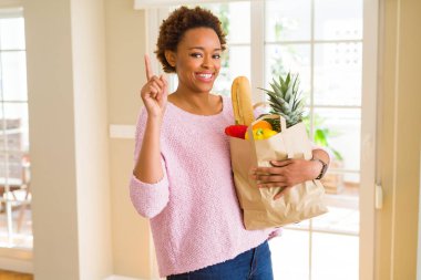 Genç Afro-Amerikan kadın holding kağıt taze yiyecek bir fikirle sürpriz dolu torba ya da gülen yüz, bir numara ile işaret parmağı soru