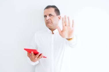 Orta yaş erkek ile beyaz duvarın üzerinden dijital tablo kullanarak açık el dur işareti ile ciddi ve kendine güvenen ifade, savunma hareketi yapıyor