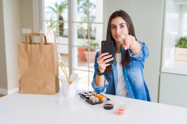 Güzel genç kadın sipariş gıda teslim kamera ve size parmak ile işaret smartphone kullanarak app el işareti, olumlu ve kendinden emin bir jest ön