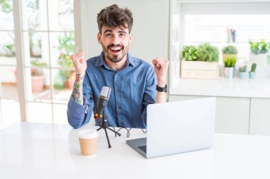Genç adam kayıt podcast mikrofon ve dizüstü kutluyor kullanarak şaşırttı ve başarı için kaldırdı Kollarını açarak hayrete ve gözleri açık. Kazanan kavramı.