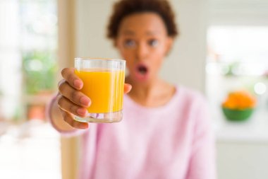 Evde bir sürpriz yüz, korkuyor ve heyecanlı korku ifadesi ile şok korkmuş genç Afro-Amerikan kadın driking portakal suyu