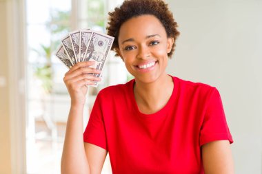 Ayakta ve diş gösterilen kendine güvenen bir gülümsemeyle gülümseyerek mutlu bir yüz ile banka notları elli dolar tutan genç Afro-Amerikan kadın