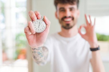 Genç adam parmak, mükemmel sembolü ile ok işareti yapıyor holding Kronometreyi kullanarak