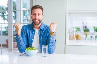 Yakışıklı adam taze sağlıklı salata kutluyor yeme şaşırttı ve başarı için kaldırdı Kollarını açarak hayret ve gözleri açık. Kazanan kavramı.