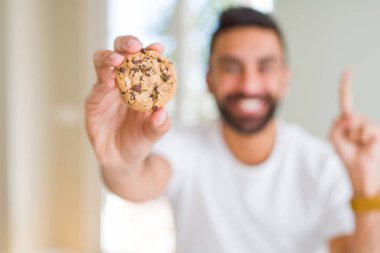 Çerezler bir fikir ya da soru işaret parmağı gülen yüz, bir numara ile sürpriz yakışıklı İspanyol adam yeme çikolata cips