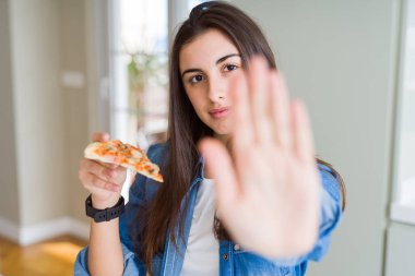 Güzel genç kadın bir dilim ile lezzetli pizza yeme dur işareti ile ciddi ve kendine güvenen ifade, savunma hareketi yaparken el açmak