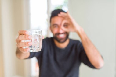 İspanyol yakışıklı mutlu yüz el parmaklarının arasından seyir göz üzerinde ok işaretiyle yapıyor gülümseyen ile taze bir bardak su içme