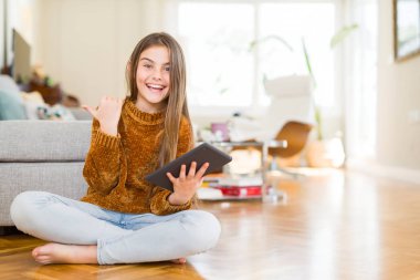 Güzel genç kız çocuk işaret ve başparmak kadar mutlu yüz gülümseyen tarafı ile gösterilen yerde oturan dijital dokunmatik tablet kullanma