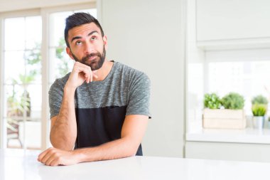 Çene düşünme hakkında soru, dalgın ifade üzerine el ile evde rahat t-shirt giyen İspanyol yakışıklı. Düşünceli yüzüyle gülümsüyor. Şüphe kavramı.