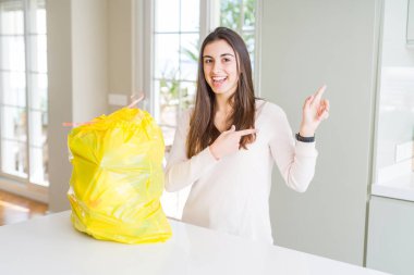 Çöp konteyner gülümseyerek gelen çöp yaptırmayı ve iki ile işaret kamera bakıyor güzel ve genç birbayan eller ve yan parmak.