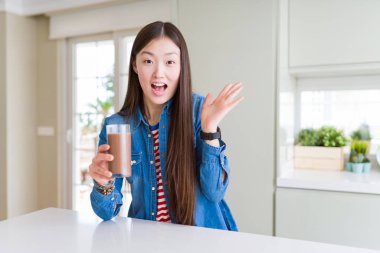 Kocaman bir gülümseme ile çığlık zaferini kutluyor ve ellerini kaldırdı çikolatalı milkshake çok mutlu ve heyecanlı, kazanan ifade taze bir kadeh içmek güzel Asyalı kadın