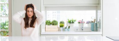 Güzel genç kadın ev umutsuz ve stresli baş ağrısı muzdarip çünkü, beyaz masada oturan geniş açı resim ağrı ve Migren. Ellerini kafasına.