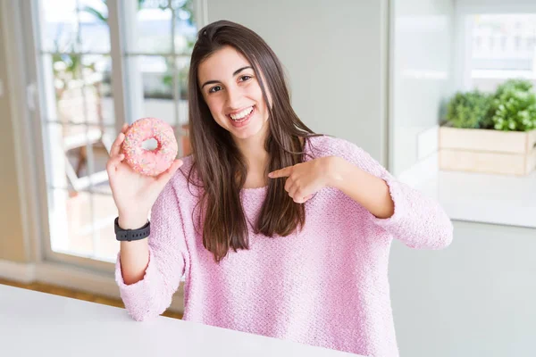 ピンクのチョコレートを食べて美しい若い女性チップ自分自身に驚き顔人差し指とドーナツ — ストック写真