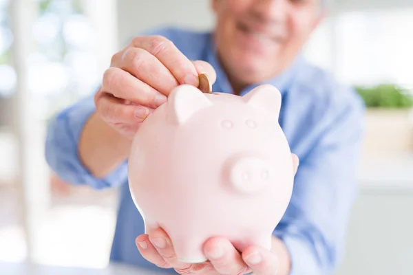 Man putting a coin inside piggy bank as savings smiling confiden