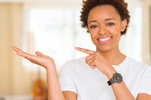 年轻美丽的非洲裔美国女人穿着休闲的白色 T恤惊讶和微笑的相机 同时提出与手和手指指指点点 — 图库照片