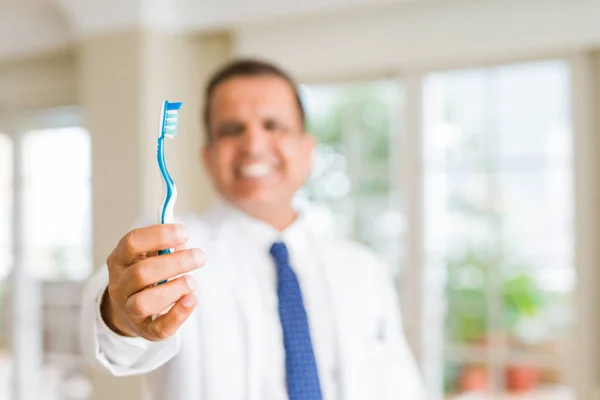 Стоматолог середнього віку чоловік тримає зубну щітку і посміхається — стокове фото