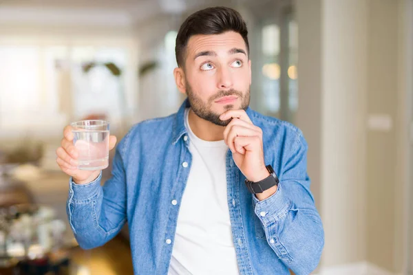 ホームの深刻な顔を考えて質問に非常に水のガラスを飲む若いハンサムな男はアイデアを混乱 — ストック写真