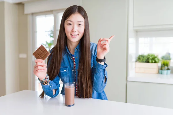 Beautiful Asian woman drinking chocolate milkshake and holding chocolate bar very happy pointing with hand and finger to the side