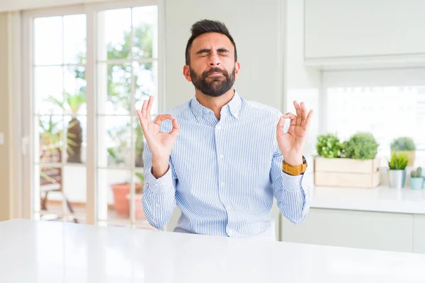 Handsome hispanic business man relax and smiling with eyes closed doing meditation gesture with fingers. Yoga concept.