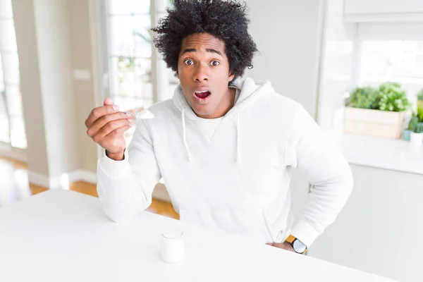 African American man eating healthy yogurt for breakfast scared in shock with a surprise face, afraid and excited with fear expression