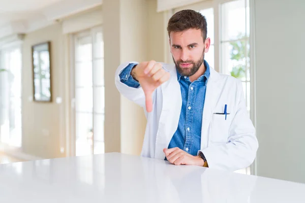 在诊所里穿着医疗外套的帅气的医生男子看上去不开心 愤怒地表现出拒绝和竖起大拇指的消极姿态 错误的表达 — 图库照片