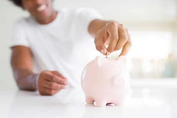 Close up of african american man saving money putting a coin inside piggy bank