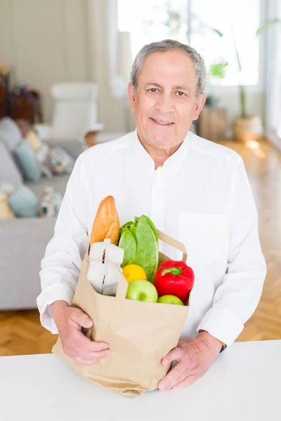 Bonito homem sênior segurando saco de papel cheio de alimentos frescos e — Fotografia de Stock