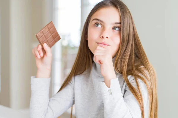 Beautiful young girl kid eating chocolate bar serious face thinking about question, very confused idea