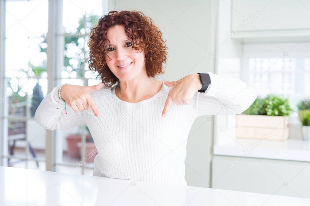 Beautiful senior woman wearing white sweater at home looking confident with smile on face, pointing oneself with fingers proud and happy.